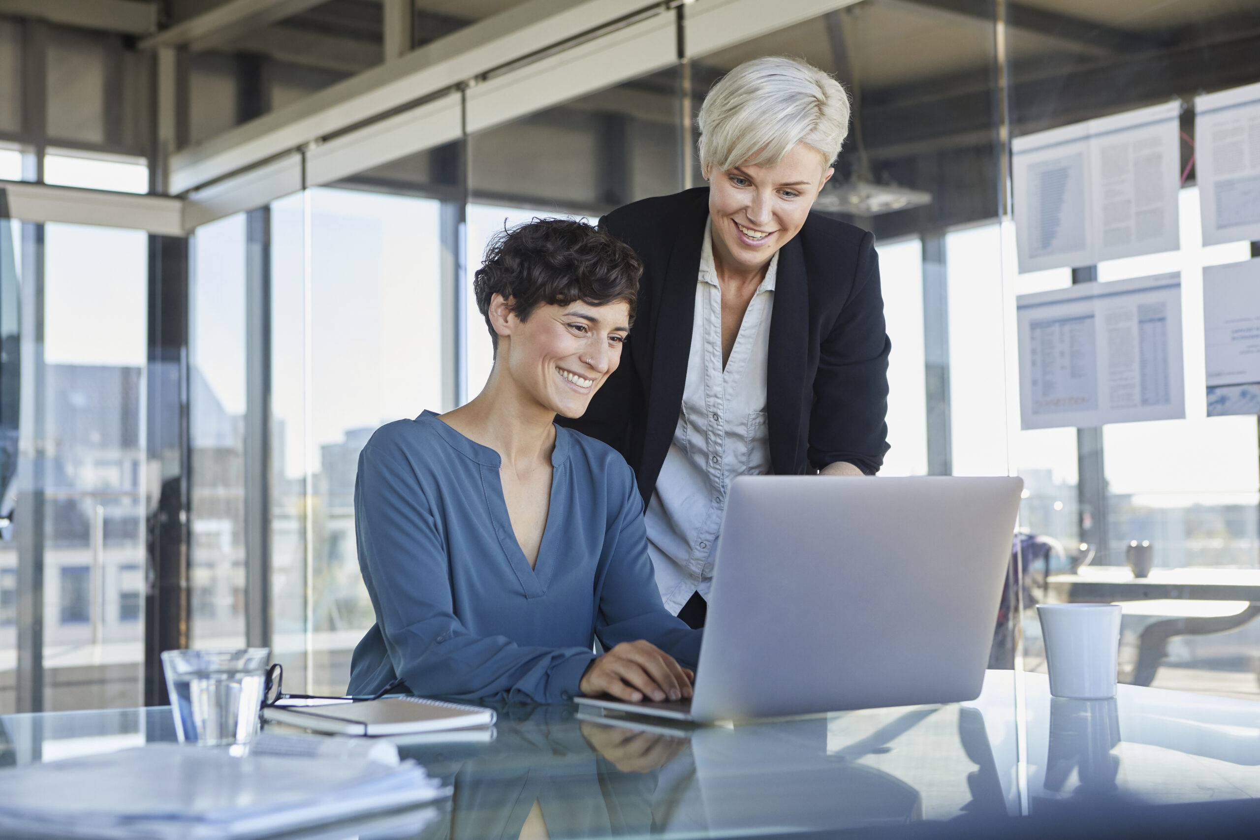 Two smiling businesswomen sharing a laptop at a desk
